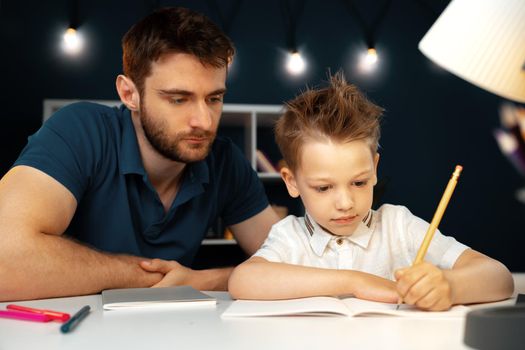 Dad and son doing school homework together sitting at the table