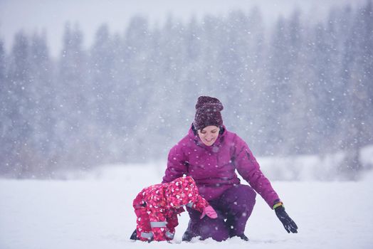 happy family on winter vacation, mom and cute little girl have fun and slide while snow falkes falling