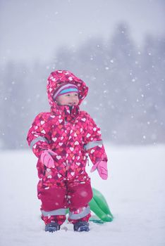 happy family on winter vacation, mom and cute little girl have fun and slide while snow falkes falling