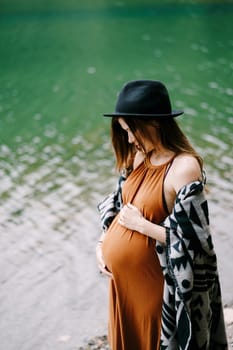 Pregnant woman hugs her belly by the lake. High quality photo