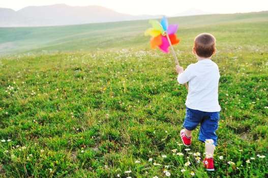 little happy child play with windmil toy and have ve fun while running on beautiful meadow at sunset