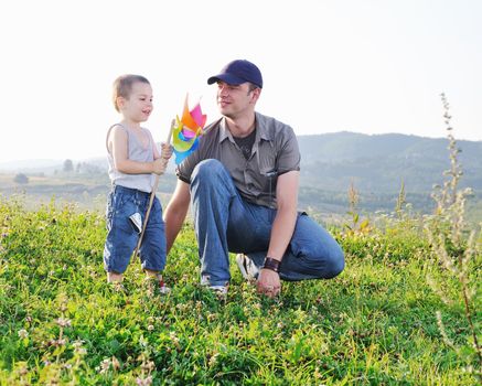 little happy child and young father  play with windmil toy and have  fun while running on beautiful meadow at sunset 