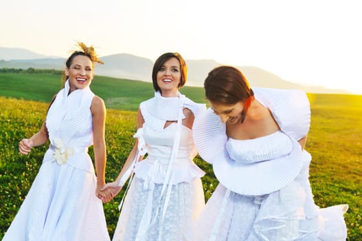 group of bride run on meadow at sunset after wedding party