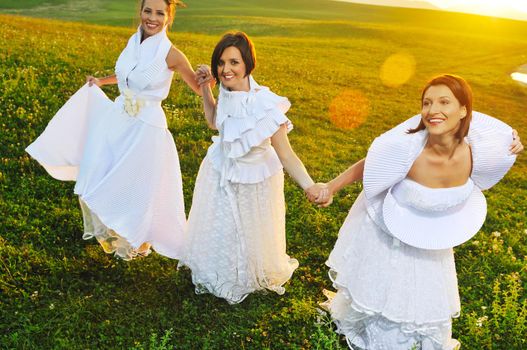 group of bride run on meadow at sunset after wedding party