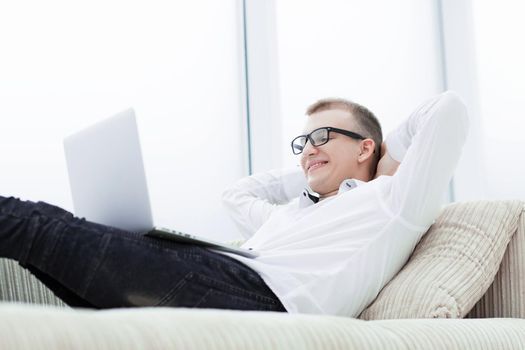 smiling man with a laptop relaxes on the sofa in his living room.photo with copy space