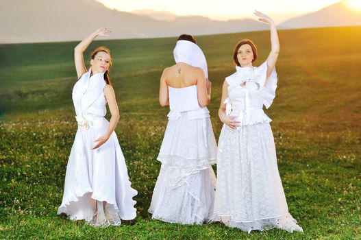 group of bride run on meadow at sunset after wedding party