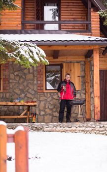young man cooking meat on barbecue in front of the weekend house on a cold winter day