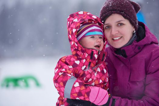 happy family on winter vacation, mom and cute little girl have fun and slide while snow falkes falling