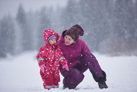 happy family on winter vacation, mom and cute little girl have fun and slide while snow falkes falling