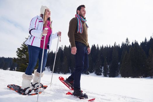 happy young  couple having fun and walking in snow shoes outdoor in nature at beautiful winter day. Health sport and relaxation