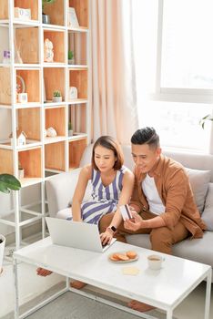 Happy couple at home paying bills with laptop and credit card