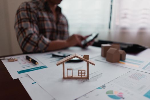 Real estate agents are calculating the house price on the table with the house model, the house purchase contract, the house design documents, the keys.