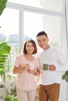 cute smiling young Asian lover couple standing near the windows in the living room in morning