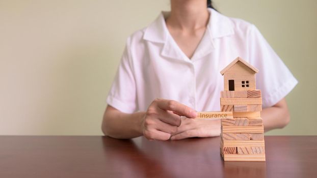 Concepts of Home Insurance and Asset Risk. Insurance agent put wooden block with message "INSURANCE"  to protect the model house.