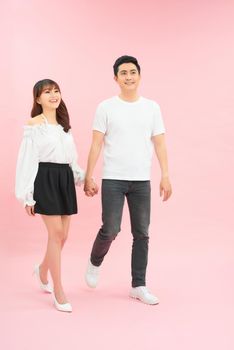 young couple walking together, going somewhere, holding hands. Isolated against pink background