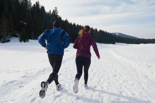 healthy young couple jogging outside on snow in forest. athlete running on  beautiful sunny winter day