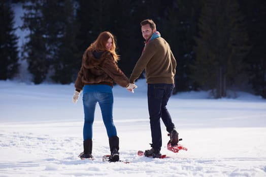 happy young  couple having fun and walking in snow shoes. Romantic winter relaxation scene