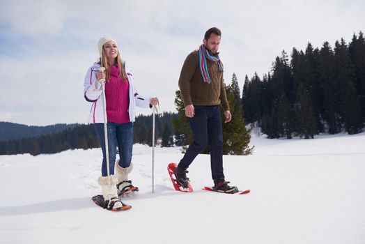 happy young  couple having fun and walking in snow shoes outdoor in nature at beautiful winter day. Health sport and relaxation