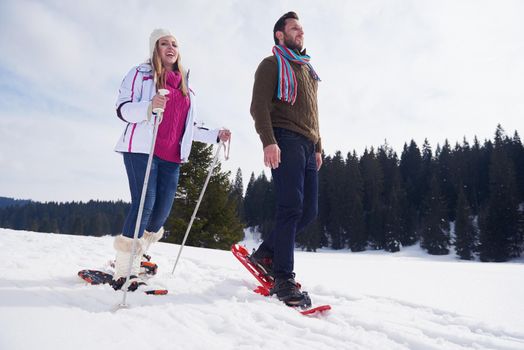 happy young  couple having fun and walking in snow shoes outdoor in nature at beautiful winter day. Health sport and relaxation