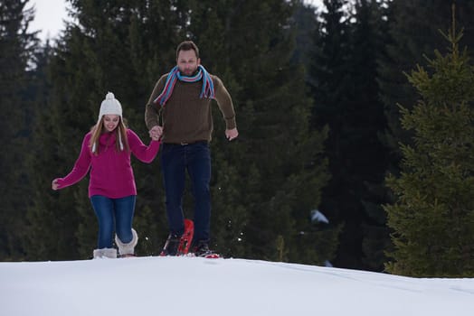 happy young  couple having fun and walking in snow shoes outdoor in nature at beautiful winter day. Health sport and relaxation