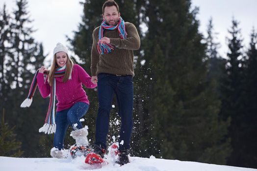 happy young  couple having fun and walking in snow shoes outdoor in nature at beautiful winter day. Health sport and relaxation