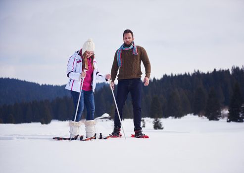 happy young  couple having fun and walking in snow shoes outdoor in nature at beautiful winter day. Health sport and relaxation