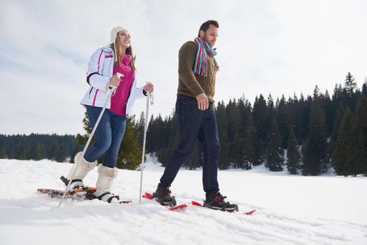 happy young  couple having fun and walking in snow shoes outdoor in nature at beautiful winter day. Health sport and relaxation