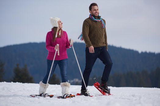 happy young  couple having fun and walking in snow shoes outdoor in nature at beautiful winter day. Health sport and relaxation