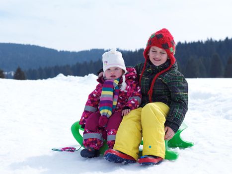 portrait of boy and baby girl on winter vacation sitting on sleddge with fresh snow on beautiful sunny day