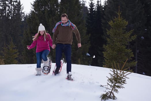 happy young  couple having fun and walking in snow shoes outdoor in nature at beautiful winter day. Health sport and relaxation