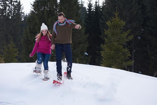 happy young  couple having fun and walking in snow shoes outdoor in nature at beautiful winter day. Health sport and relaxation