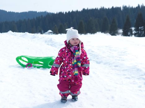 little baby girl have fun on fresh snow and slide on sleddges at beautiful sunny winter day