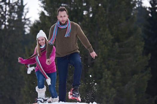 happy young  couple having fun and walking in snow shoes outdoor in nature at beautiful winter day. Health sport and relaxation