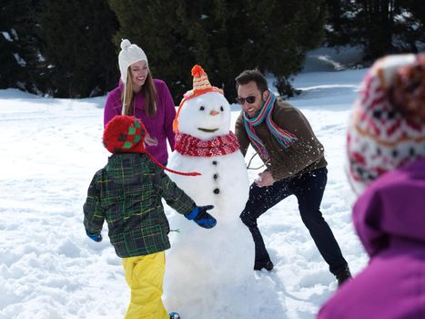 happy young  family playing in fresh snow and making snowman at beautiful sunny winter day outdoor in nature with forest in background