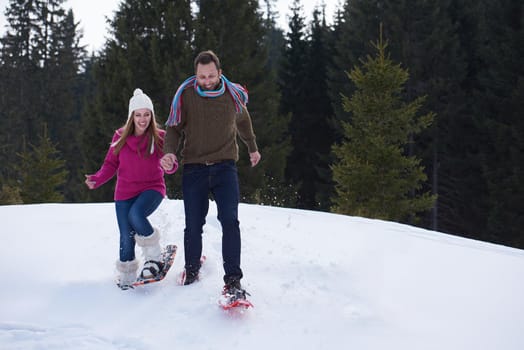 happy young  couple having fun and walking in snow shoes outdoor in nature at beautiful winter day. Health sport and relaxation