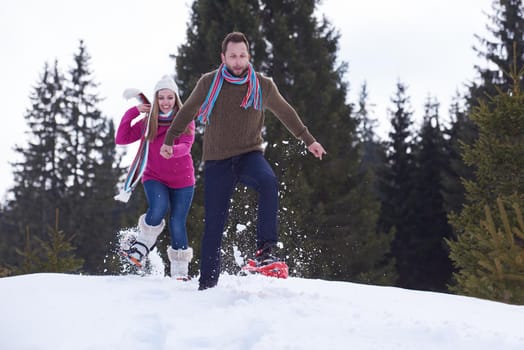 happy young  couple having fun and walking in snow shoes outdoor in nature at beautiful winter day. Health sport and relaxation