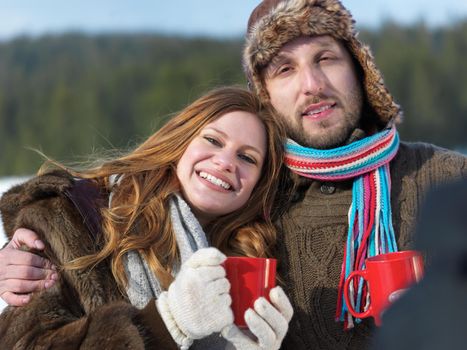 portrait of happy young couple outdoor on winter day drinking warm tea with fresh snow in background