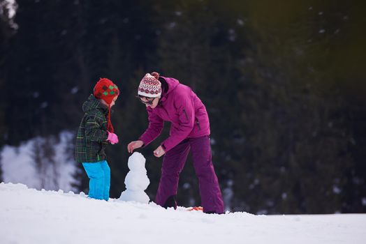 happy young  family playing in fresh snow and building snowman at beautiful sunny winter day outdoor in nature