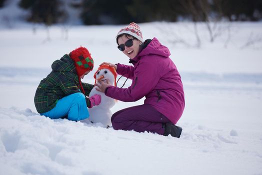 happy young  family playing in fresh snow and building snowman at beautiful sunny winter day outdoor in nature