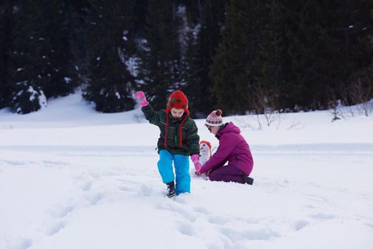 happy young  family playing in fresh snow and building snowman at beautiful sunny winter day outdoor in nature