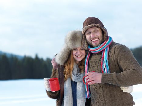 portrait of happy young couple outdoor on winter day drinking warm tea with fresh snow in background