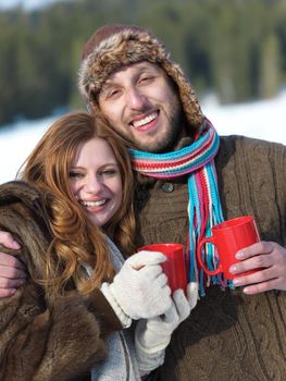 portrait of happy young couple outdoor on winter day drinking warm tea with fresh snow in background