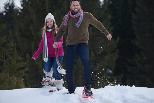 happy young  couple having fun and walking in snow shoes. Romantic winter relaxation scene