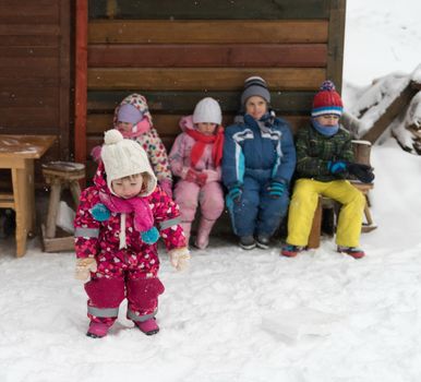 group portrait of kids, little child  group sitting together  in front of wooden cabin on vacation at beautiful winter  day with fresh snow