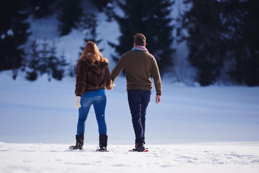 happy young  couple having fun and walking in snow shoes. Romantic winter relaxation scene