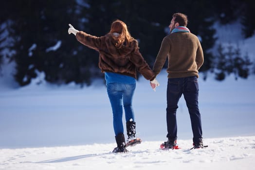 happy young  couple having fun and walking in snow shoes. Romantic winter relaxation scene