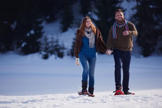 happy young  couple having fun and walking in snow shoes. Romantic winter relaxation scene