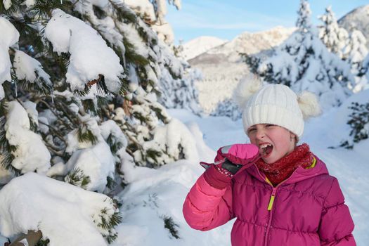 portrait of cute little girl  while eating icicle  on beautiful winter day with fresh snow