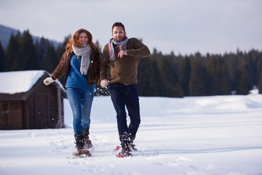 happy young  couple having fun and walking in snow shoes. Romantic winter relaxation scene