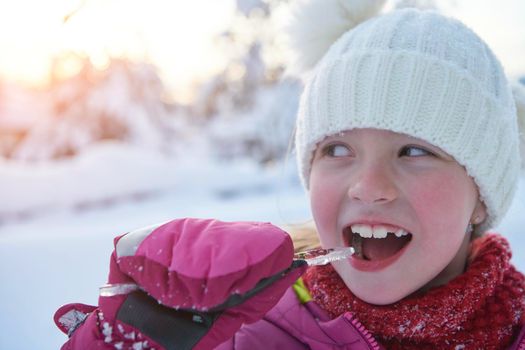 portrait of cute little girl  while eating icicle  on beautiful winter day with fresh snow